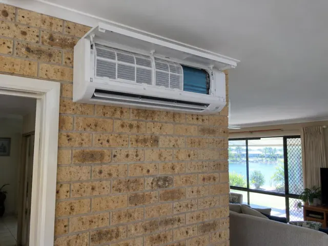 Clean split system mounted high on a brick wall in a living room with open front panel in Varsity Lakes