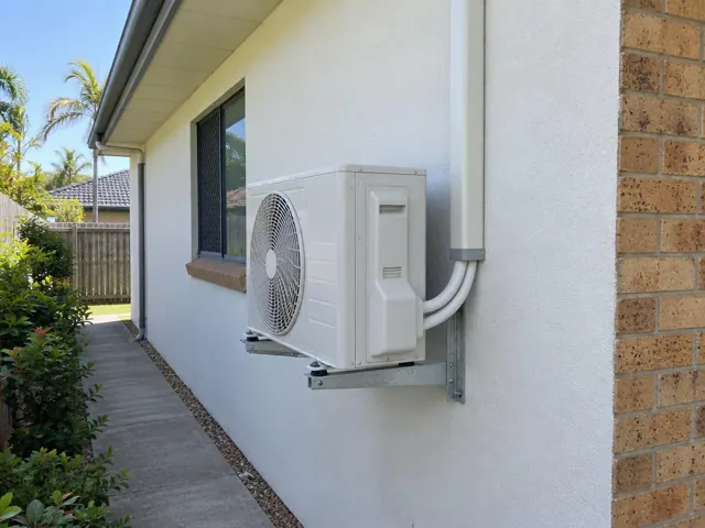 Outdoor air conditioner unit mounted on a house wall beside a window in Robina