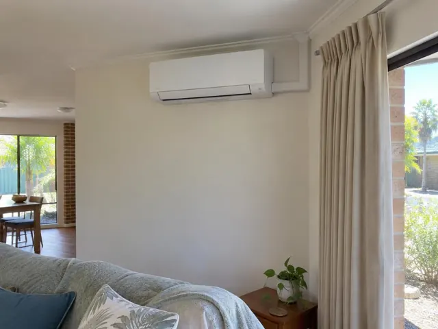 White split system mounted high on a living room wall beside curtains and a window in Burleigh Waters